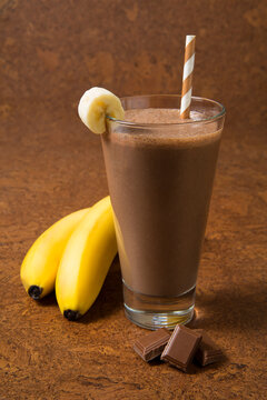 
Chocolate banana smoothie in a glass with ingredients on a brown background. Selected focus.
