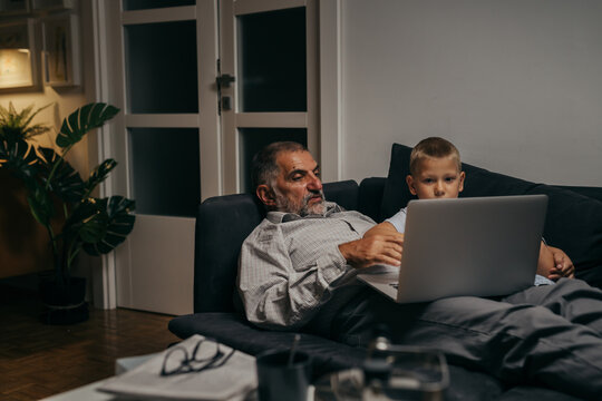 grandfather and grandson laying on the sofa and using laptop computer at home