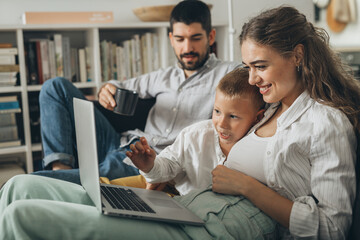Obraz premium happy young family using laptop computer sitting on the sofa at home