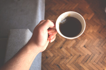 Hand holding a cup of tea on a gray armchair