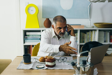 middle age man sitting at the dinning table, having breakfast and using laptop computer