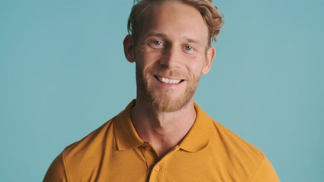 Attractive smiling blond bearded man happily looking in camera over colorful background