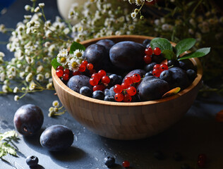 Ripe summer berries in a wooden bowl on a dark background