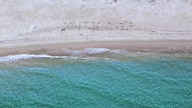 Aerial view of dont send help message written on sand beach