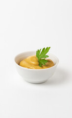 Mustard sauce decorated with parsley in a small white bowl on a white background