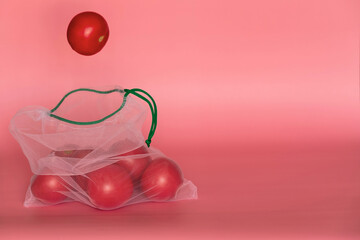 The reusable organza net bag for shopping with falling tomato into it are on the pink background. Concept of no plastic, zero waste, reusable life. Flat lay. Copy space.