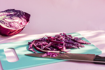 Fresh red cabbage sliced and chopped on turquoise cutting board on pink backgroud. Vegetable for...