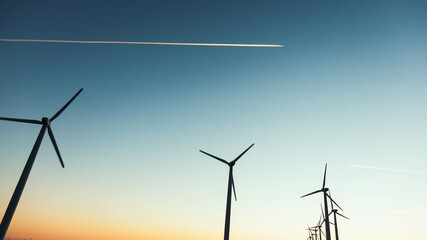 Fototapeta premium Wind Turbines at Dusk. Landscape sunset with windmills. Renewal source of electricity. Wind turbines field new technology for clean energy on mountain, sunset view with colorful twilight on sky.