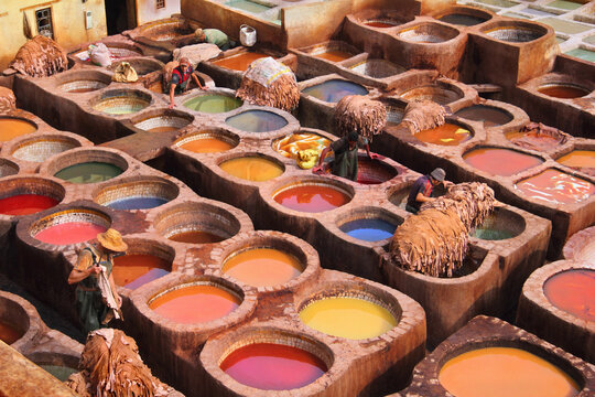 Round stone vessels with dye liquids and unidentified men work at the famous Chouara Tannery in historical center, ancient Medina of Fes, Morocco, North West Africa.