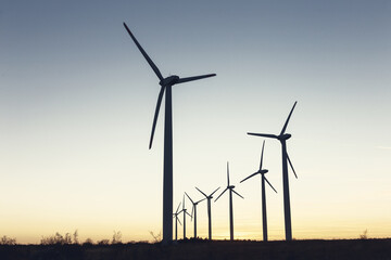 Fototapeta premium Wind Turbines at Dusk. Landscape sunset with windmills. Renewal source of electricity. Wind turbines field new technology for clean energy on mountain, sunset view with colorful twilight on sky.