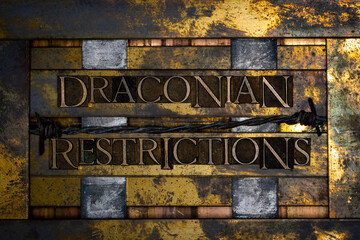 Draconian Restrictions  text formed with real authentic typeset letters with barbed wire on vintage textured silver grunge copper and gold background
