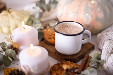 Hot cocoa with cookies in a white mug surrounded by autumn leaves and pumpkins