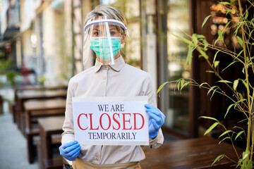 Female owner holding closed sign at outdoor cafe due to coronavirus pandemic.