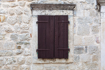 Fototapeta na wymiar Closed brown wooden window shutters on an beautiful old stone seaside house.