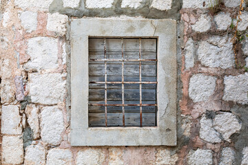 Fototapeta na wymiar Weathered closed window with rusty bars on an old abandoned stone seaside house.
