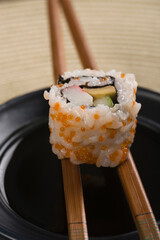 Close-up of a maki sushi with chopsticks on a bowl