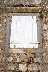 Weathered closed white window shutters on an old abandoned stone seaside house.