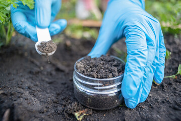 A soil science concept. Scientist is holding in hands a jar with soil sample and scoop. - obrazy, fototapety, plakaty