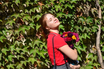 Beautiful young woman with a bouquet of flowers near a green wall of bushes. Floral business. Copy space.