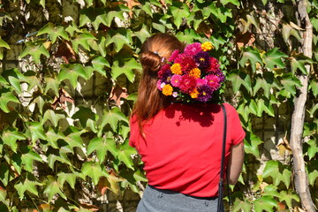 Beautiful young woman with a bouquet of flowers near a green wall of bushes. Floral business. Copy space.