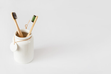 Ceramic cup with wooden toothbrushes on white with copy space. Ecological material and dental care