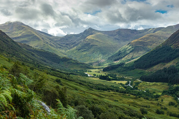 Fototapeta na wymiar Dramatic Glen Nevis view with mountains in distance and lush valley, cloudy with patches of blue sky