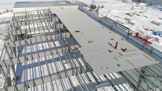 Workers roof plant warehouse at snowy construction site