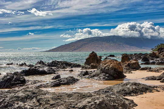 Lava rock and sand at Charley Young Beach with the West Maui Mountains in the distance