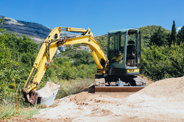 Excavator with a bucket extracts sand in a sand quarry - sunny day in the mountains