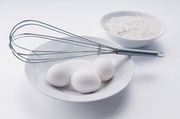 Eggs and wire whisk with a bowl of flour