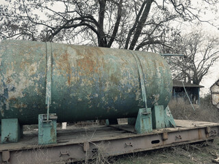 Large rusty metal water tank with remains of blue and green paint. Old big rusty automobile water tank with traces of rust. Abandoned waste rusty painted metal car tank, water barrel.