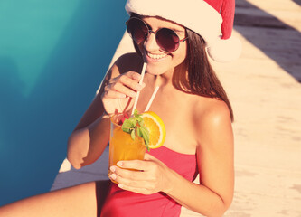 Young woman in Santa Claus hat with refreshing drink near swimming pool. Christmas vacation