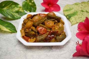 Top view of Indian vegetable curry Bhindi do pyaza made of whole big pieces of lady fingers and onions, a side dish north indian punjabi style gravy ki sabji. Decorated with flowers and leaves