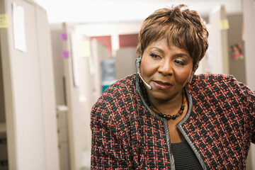 Serious Black businesswoman standing in office talking on headset