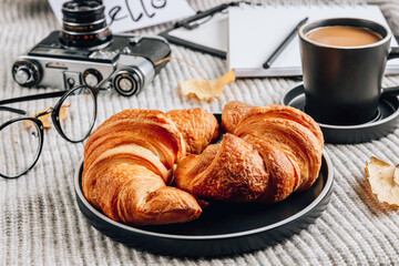 Fresh croissant and cup of coffee on a gray knitted background. Cozy autumn morning breakfast composition