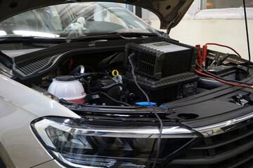 A modern car in a car service at a diagnostic post. The hood is open on the vehicle and diagnostic equipment is connected.