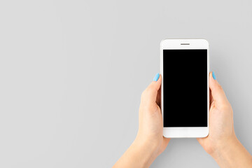 Female hands using smartphone with empty screen on gray background. Top view. Banner