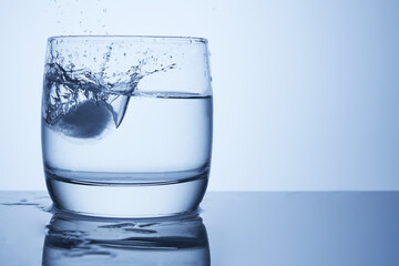 Ice falls into a glass of water with splashes, drops and air bubbles.