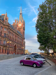 Fototapeta na wymiar The clock tower of the famous Kings Cross St Pancras railway station and old car parking in London, England