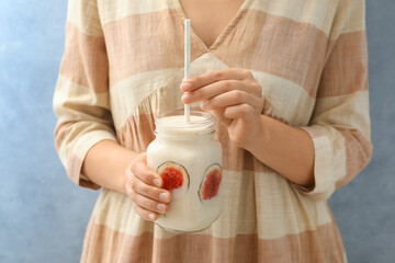 Woman holding mason jar with fig smoothie on light blue background, closeup