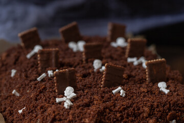 Kuchen als Friedhof mit Gräbern und Skeletten aus Schokokrümel, Creme und Banane auf Tisch aus Holz und dahinter Spinnweben