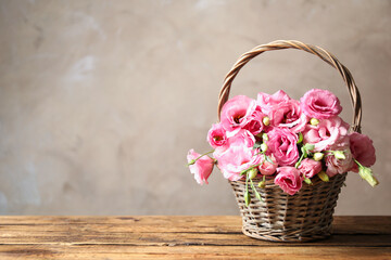 Fototapeta na wymiar Beautiful pink Eustoma flowers in wicker basket on wooden table against grey background. Space for text