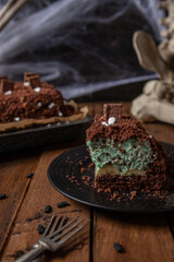 Kuchen als Friedhof mit Gräbern und Skeletten aus Schokokrümel, Creme und Banane auf Tisch aus Holz und dahinter Spinnweben