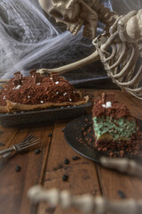 Kuchen als Friedhof mit Gräbern und Skeletten aus Schokokrümel, Creme und Banane auf Tisch aus Holz und dahinter Spinnweben