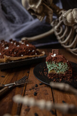 Kuchen als Friedhof mit Gräbern und Skeletten aus Schokokrümel, Creme und Banane auf Tisch aus Holz und dahinter Spinnweben