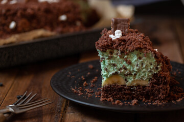 Kuchen als Friedhof mit Gräbern und Skeletten aus Schokokrümel, Creme und Banane auf Tisch aus Holz und dahinter Spinnweben