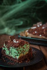 Kuchen als Friedhof mit Gräbern und Skeletten aus Schokokrümel, Creme und Banane auf Tisch aus Holz und dahinter Spinnweben