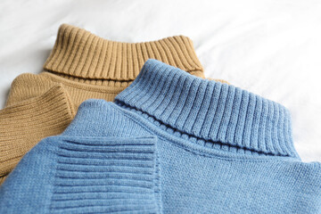 Stylish knitted sweaters on white fabric, closeup