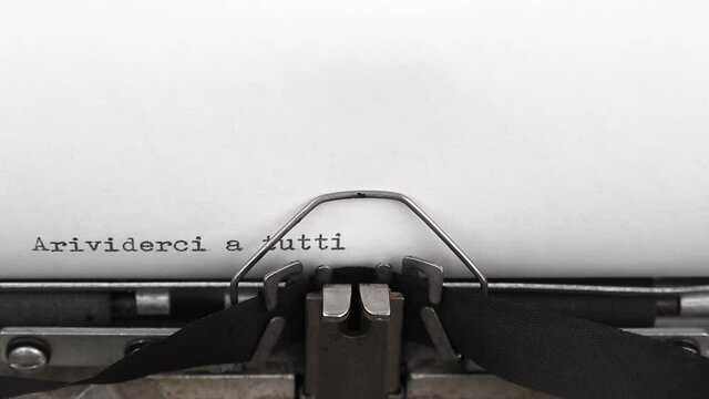 typing a message on italian arrivederci a tutti on a vintage typewriter close-up. translation from italian into english - goodbye everyone