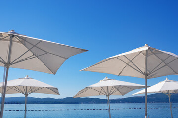 Beach vacation concept. White sun umbrellas on blue sky background. Montenegro,  view of Kotor Bay near Tivat city. Free space for text